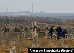 Люди відвідують могилу на Маріупольському кладовищі, 9 листопада 2022 року. Вважається, що десятки тисяч людей загинули під час майже тримісячної облоги Маріуполя російською армією