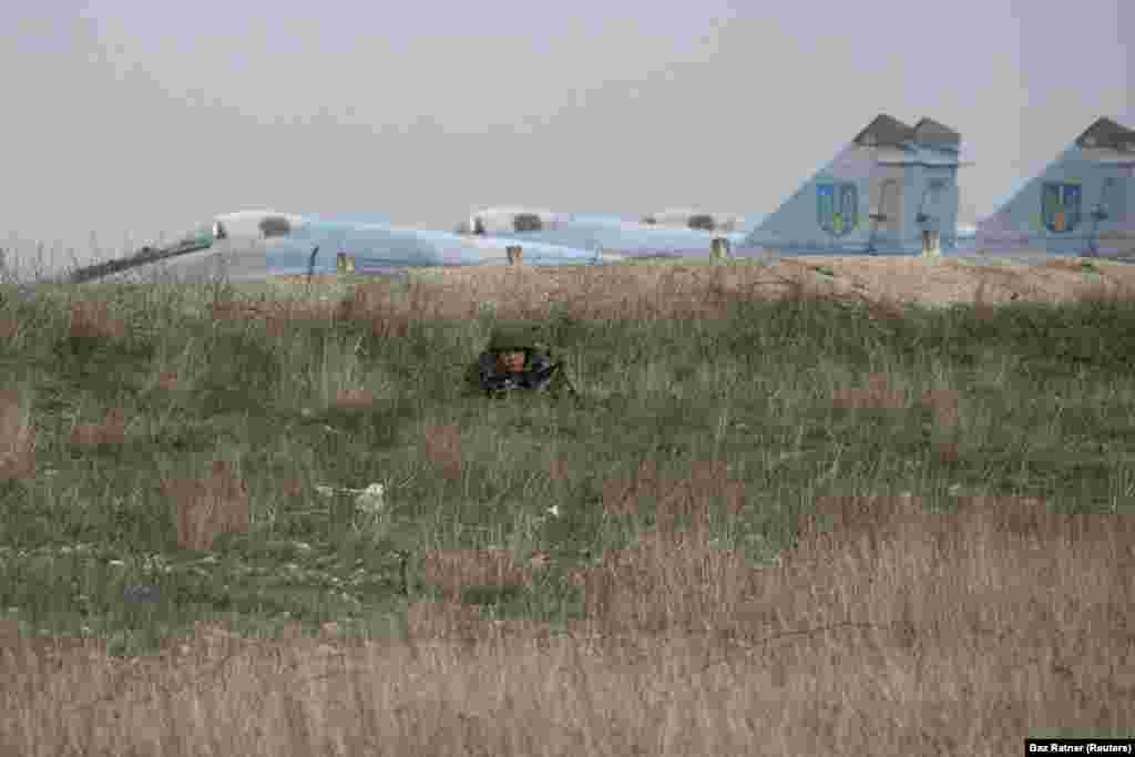 Российский солдат наблюдает за украинскими военнослужащими в аэропорту Бельбек под Севастополем. База ВВС Украины стала одним из последних украинских оплотов в Крыму, поскольку ее командир отказался передать ее российским войскам. В конце концов он был задержан российскими войсками, а украинский воинский персонал был выдворен.