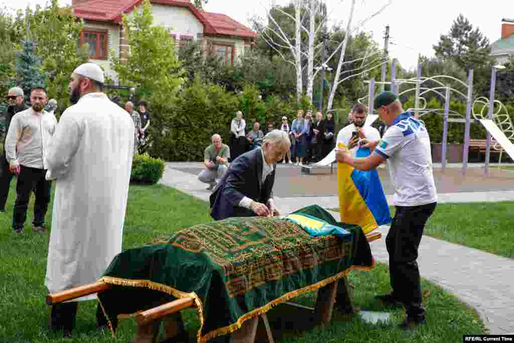 Церемония прощания с Айдосом Садыковым прошла в селе Чайки под Киевом. Организацию похорон взяла на себя крымскотатарская община, с представителями которой дружил покойный. На фото: лидер крымских татар Мустафа Джемилев (в центре) укрывает тело Айдоса Садыкова флагом Казахстана. Киевская область, 5 июля 2024 года 