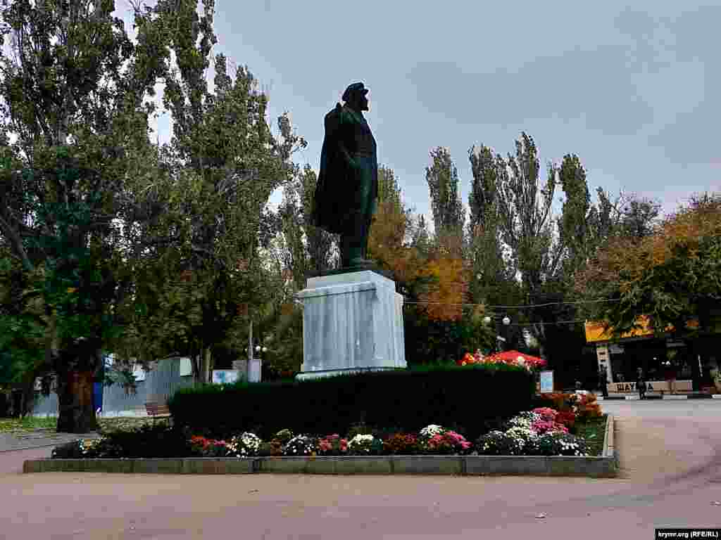 Разноцветная листва на деревьях и цветы на клумбе возле памятника Ленину в Феодосии – последние краски уходящей осени в Крыму