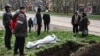 Мариуполдо көз жумган адамдын сөөгүн көчө боюнда жерге берип жатышат. 