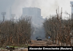 Бронемашина російських військ рухається по зруйнованій вулиці в Маріуполі, 12 квітня 2022 року. На задньому плані видно металургійний завод «Азовсталь», який у повному оточенні утримували українські військові