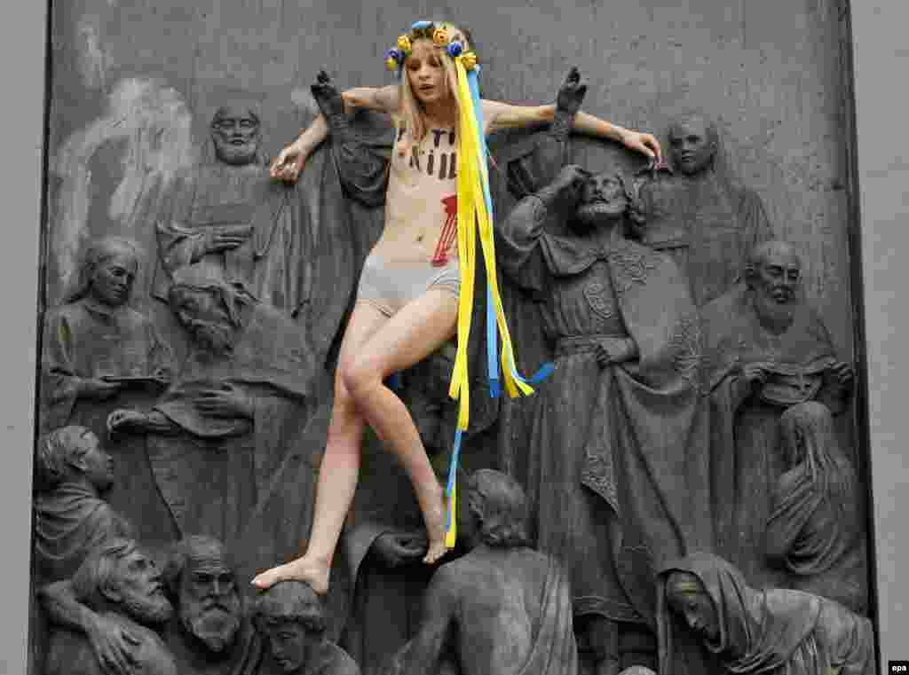 Активістка Femen Анна Алляйн вилізла на пам’ятник Київському князеві Володимиру із написом на грудях «Путін вбиває», Київ, 27 липня 2017 року. У заяві організації Femen зазначено, що цей жест символізує розп’яття. «Хода Московського патріархату вулицями Києва – це «тихий марш» кремлівського агресора, після якого можуть прийти танки», – наголошують у Femen. БІЛЬШЕ ПРО ЦЕ