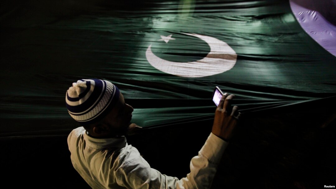 A supporter of the religious party Jamaat-e Islami takes pictures with a mobile phone as he holds Pakistan's national flag during an election campaign rally in Karachi.