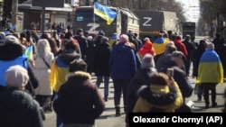 Демонстранти з прапорами України йдуть до вантажівок російської армії під час акції проти російської окупації. Херсон, 20 березня 2022 року