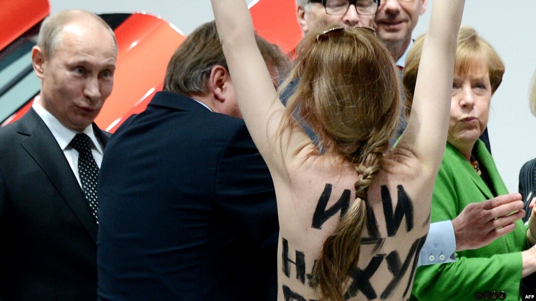 A topless demonstrator with a message on her back walks toward Russian President Vladimir Putin (left) and Chancellor Angela Merkel (right) during their visit to the industrial fair in Hannover on April 8.
