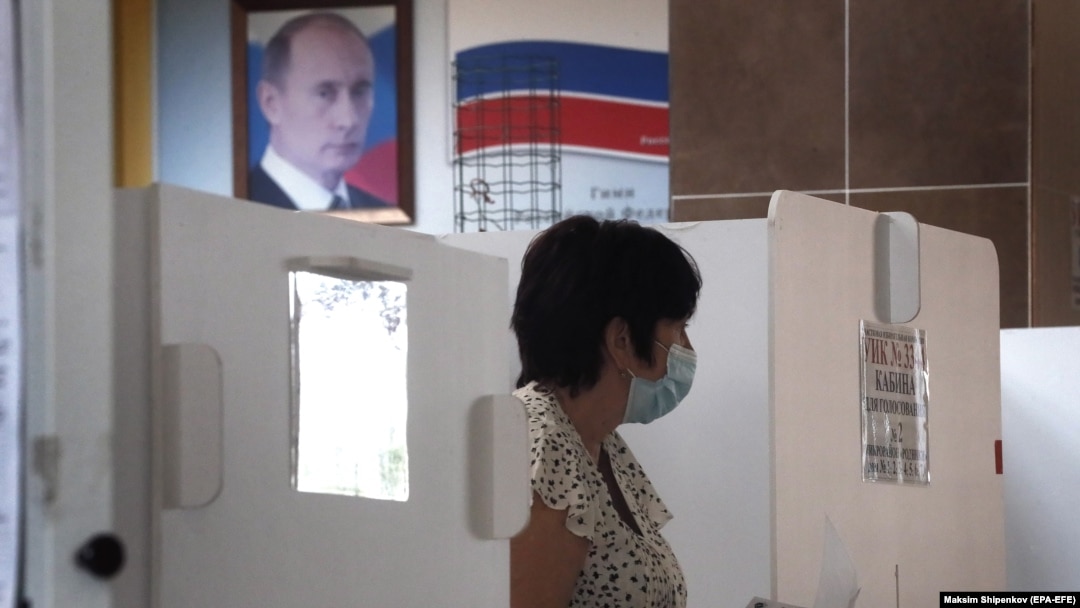 With a portrait of President Vladimir Putin in the background, a woman in Moscow prepares to cast her ballot during early voting in a controversial plebiscite on amendments to the Russian Constitution. 